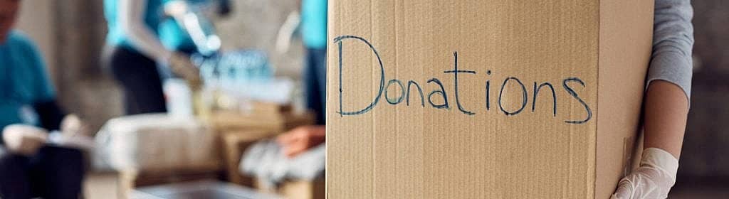Close up of woman holds cardboard box filled with donated clothes while volunteering at charity center.