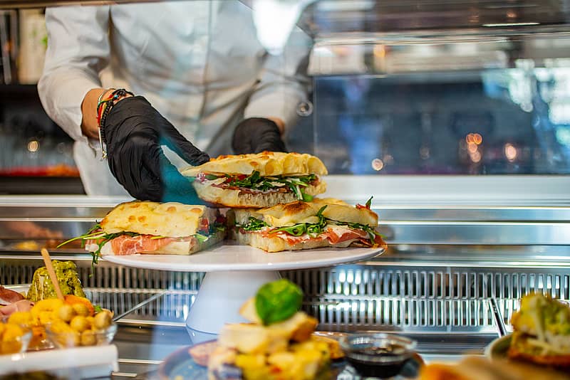 a chef stacks sandwiches on a raised plate inside of a glass display case 
