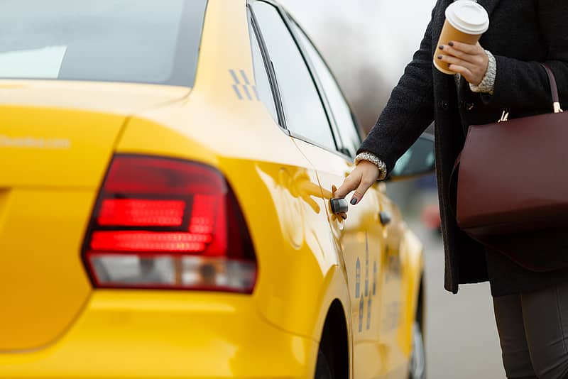 Girl with coffee in hand opens door of yellow taxi