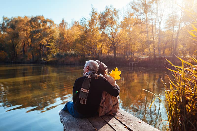 older couple enjoying time together sitting on a dock by a relaxing lake
