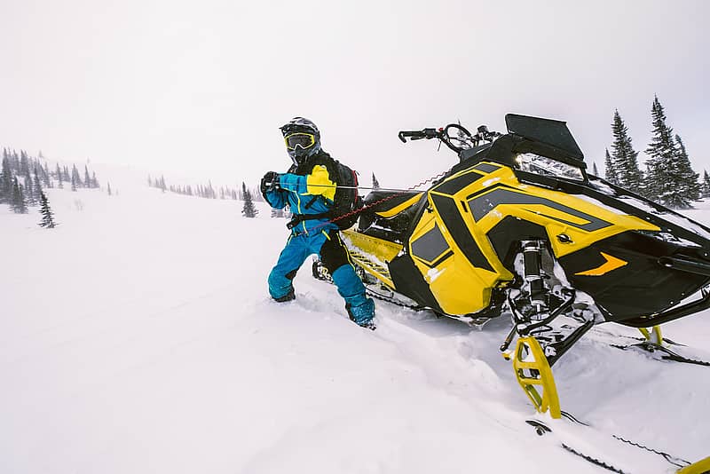 snowmobile rider pulling cord to start his snowmobile in snowy climate