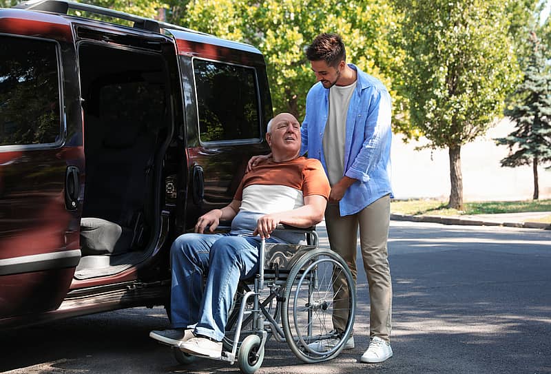 man helping patient transfer from wheelchair to a van