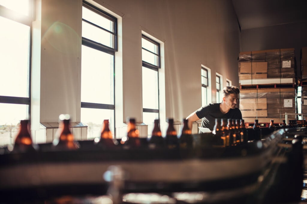 image showing employee inspecting beer bottles near conveyer belt