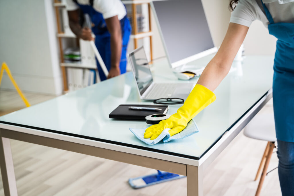 a cleaning company employee cleans the surface of a desk in an office 