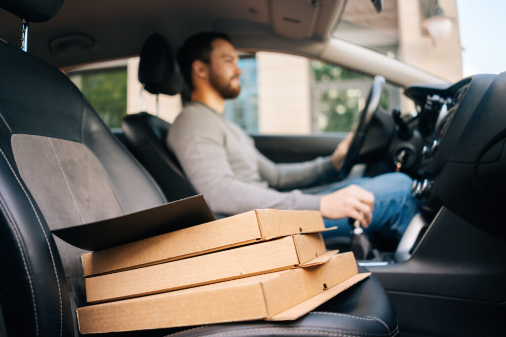 a pizza delivery driver with a stack of pizzas in the front seat of his car 