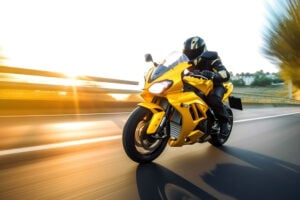 a person riding a yellow motorcycle on a road with blurry trees in the background of the picture and the sun shining on the road