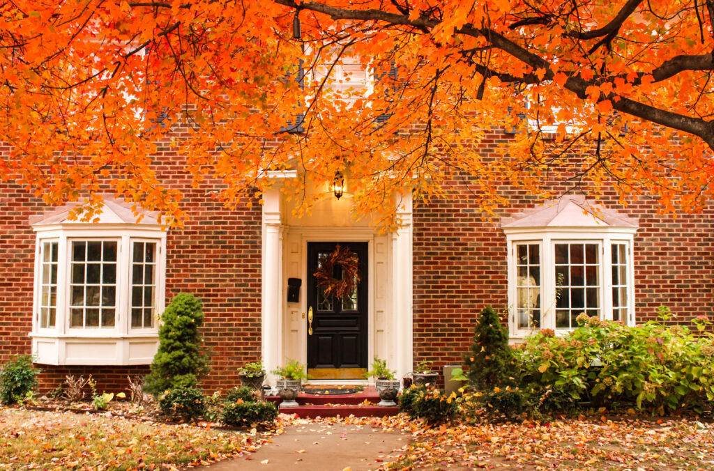 front of red brick historic home with bay windows, fall leaves are on the ground 