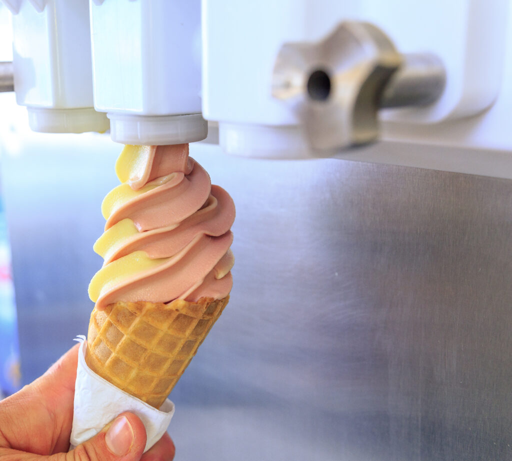 a worker dispenses ice cream into a cone from a soft serve machine in an ice cream shop