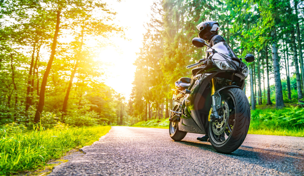 image of biker standing with his motorcycle in wooded trail